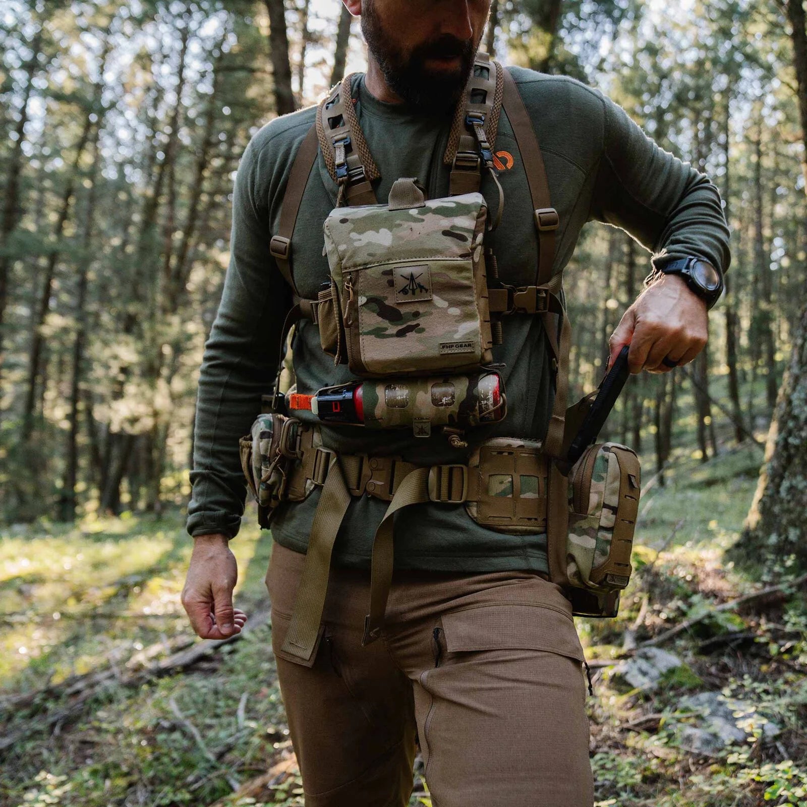 Multicam chest rig with tan straps, multiple pouches, and bear spray, worn in a forest.