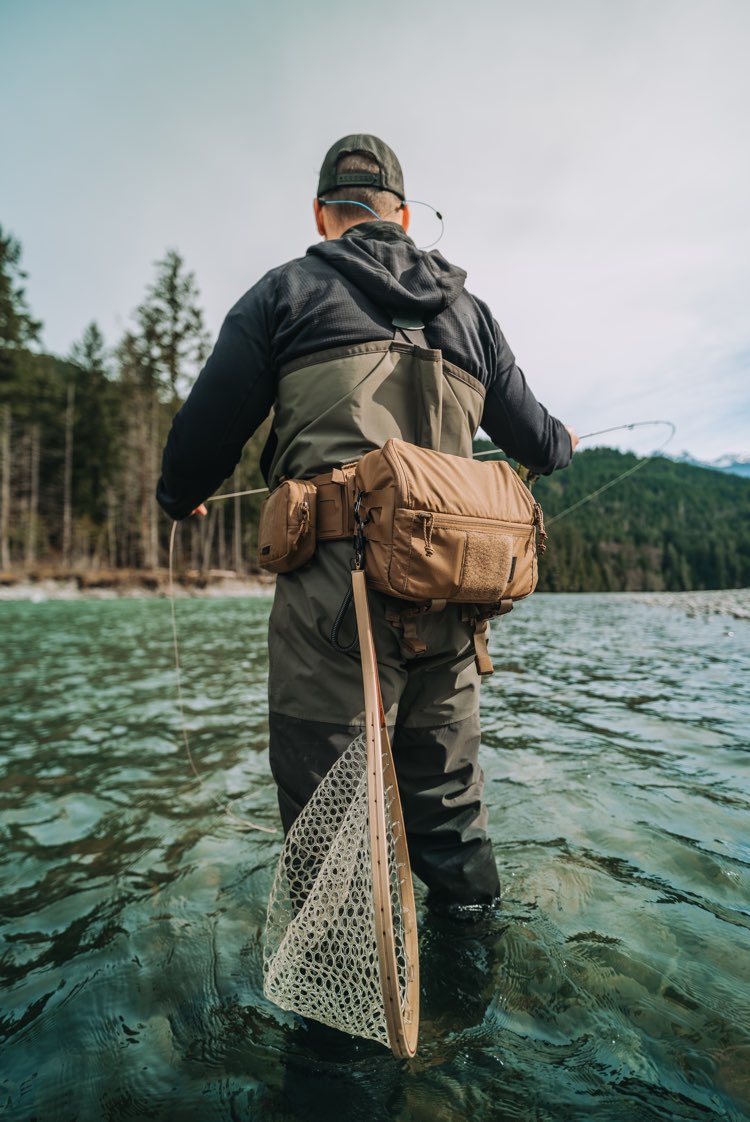 Person fly fishing in a serene lake surrounded by trees