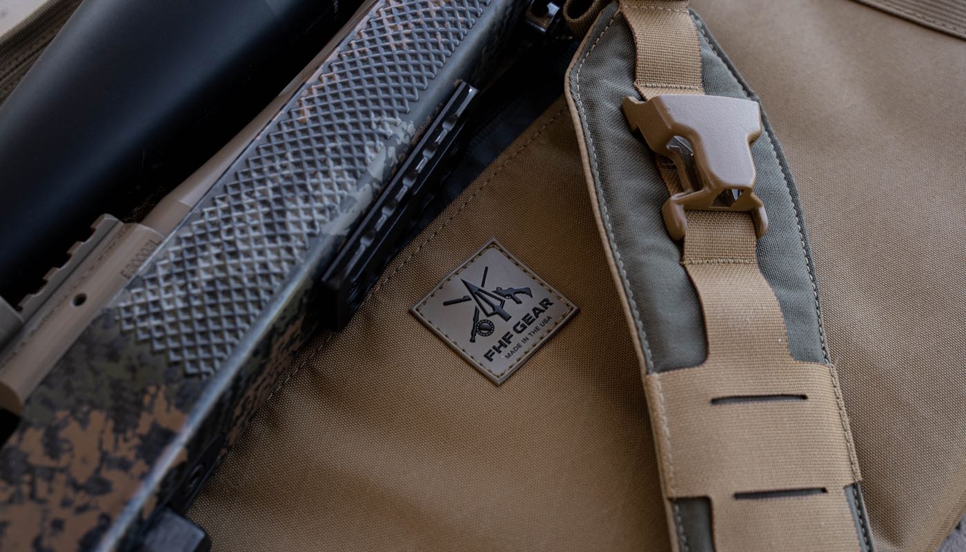 Close-up of a tactical rifle with a sling and a visible brand patch on a brown background.