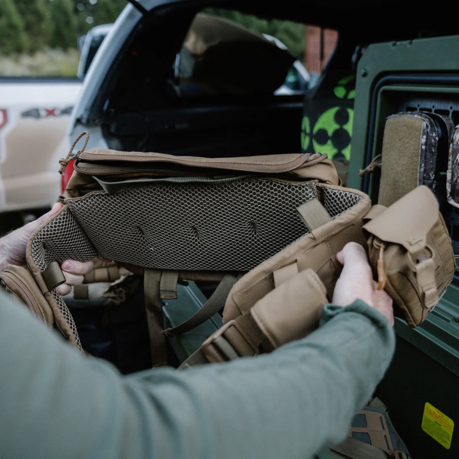 Hands holding a tan tactical waist belt with mesh padding and multiple pouches.