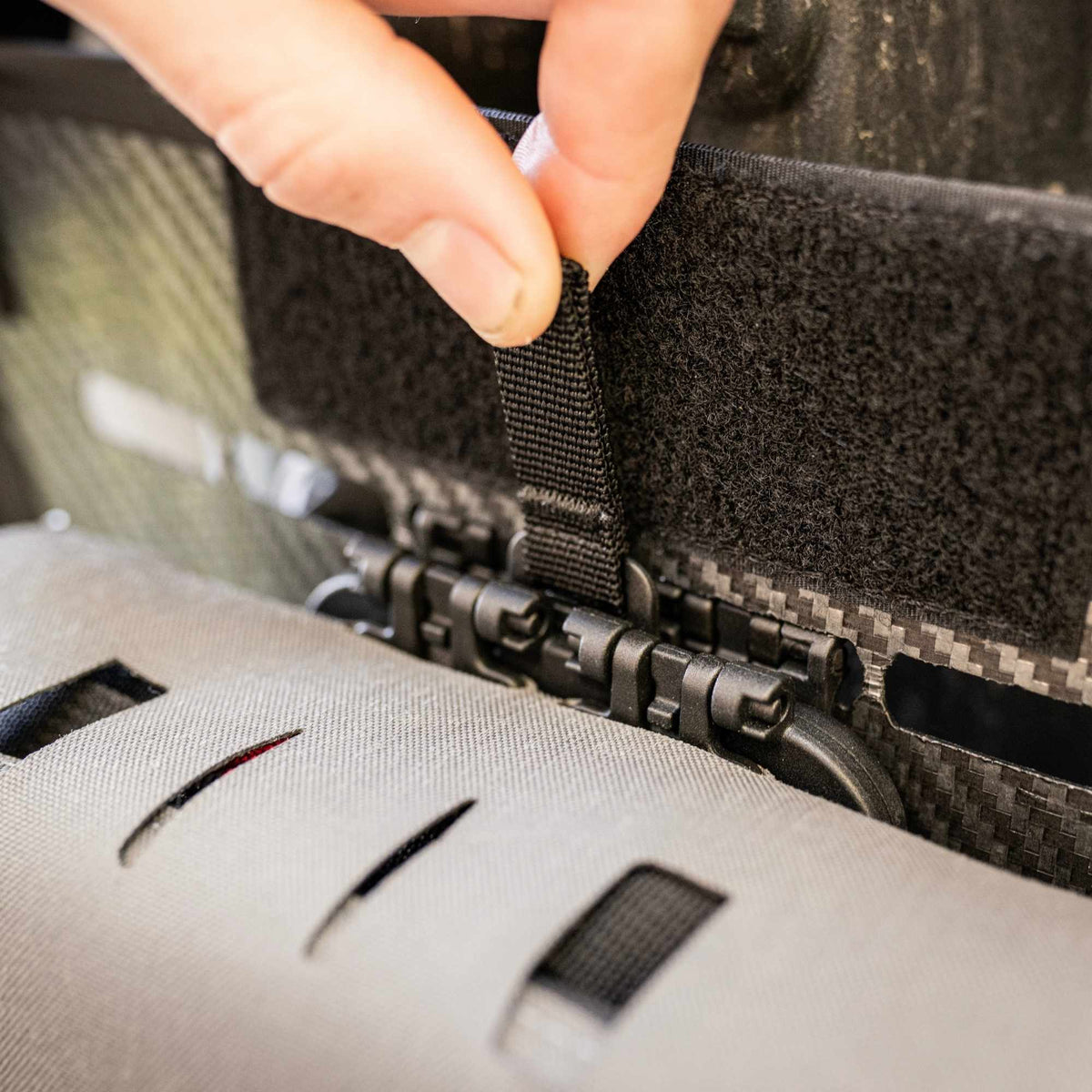 Man securing a grey pouch to a multi-point webbing strap with a to a black Snapcor buckle.