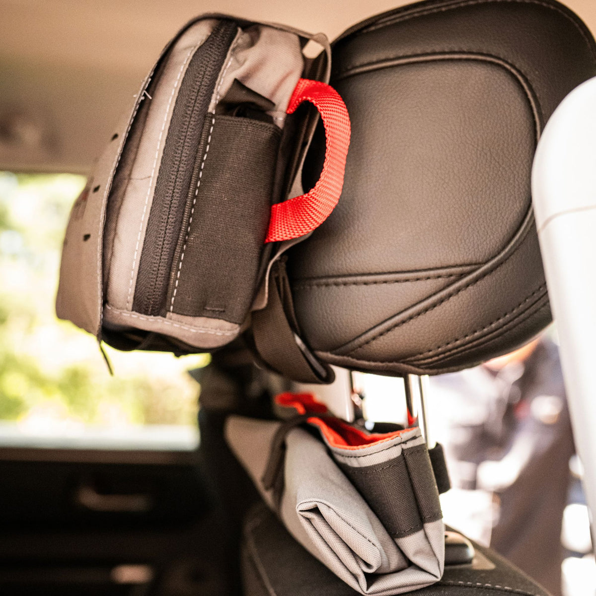 Grey medical kit and a rolled up grey storage bag mounted at the back of a black headrest.