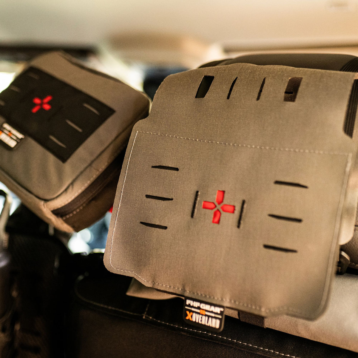 Couple of grey medical kit on a headrest with an orange cross in the center of each and showcasing FHF GEAR XOVERLAND branding.