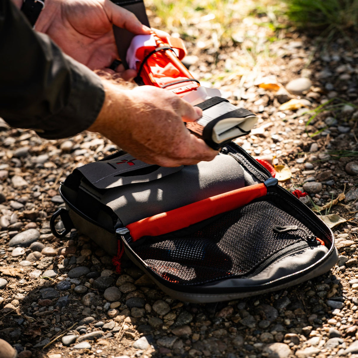 Man holding medical accessories on the field and a medical kit on the ground open showing the interior of it.