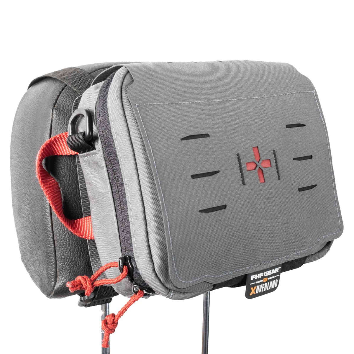 Grey medical kit hold on a headrest, it has orange cords on zippers, an orange strap on the side, an orange cross in the middle and a tag with FHF GEAR XOVERLAND branding.