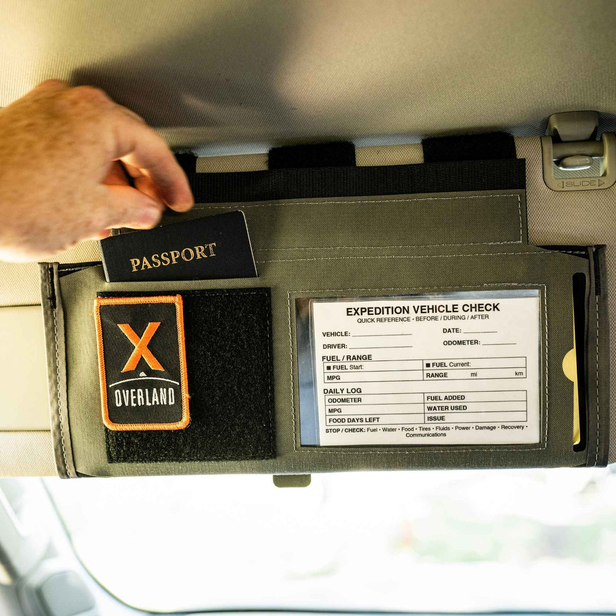 Gray car visor organizer mounted and a hand putting in a passport in a small puoch.