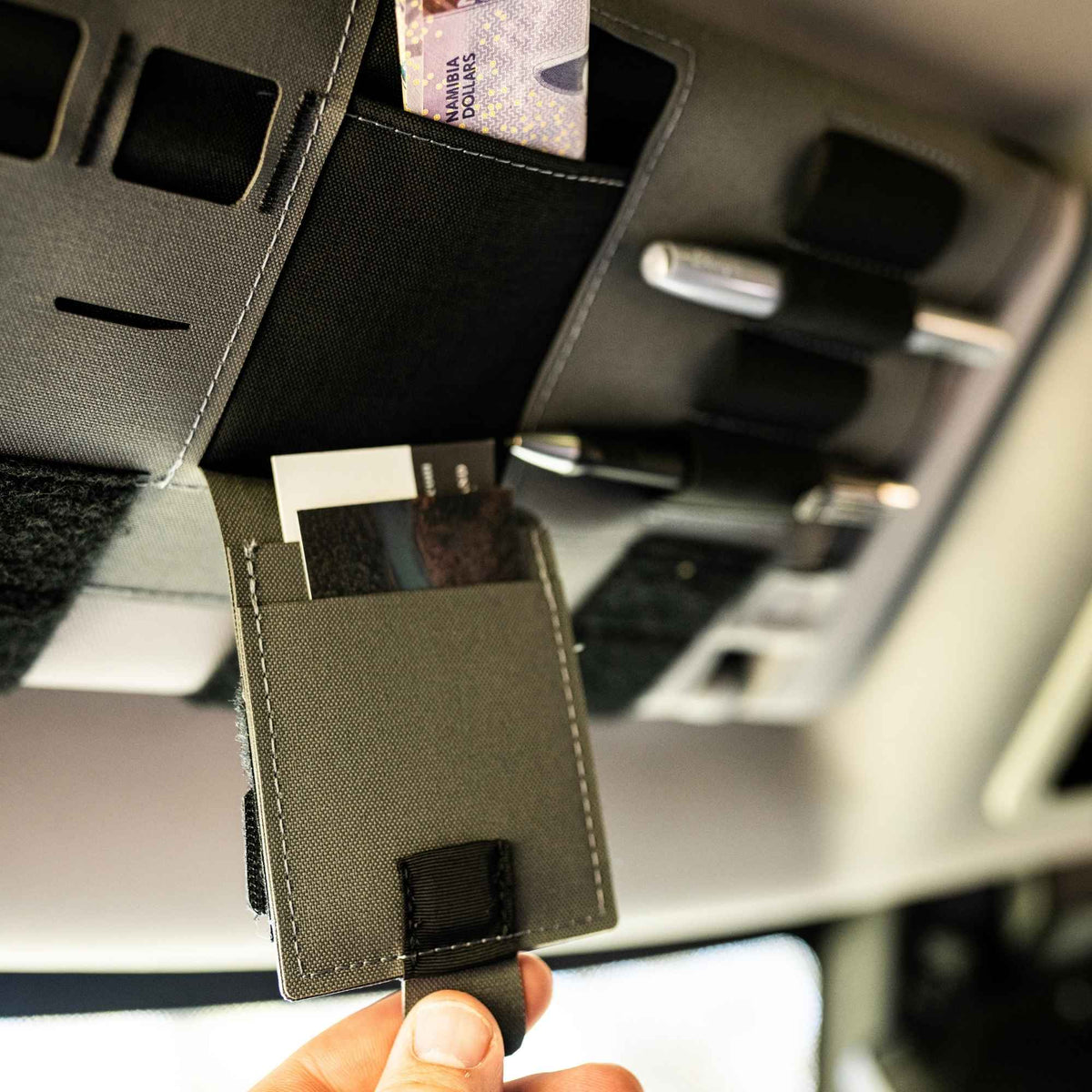 Fingers pulling a patch of a gray car visor organizer.