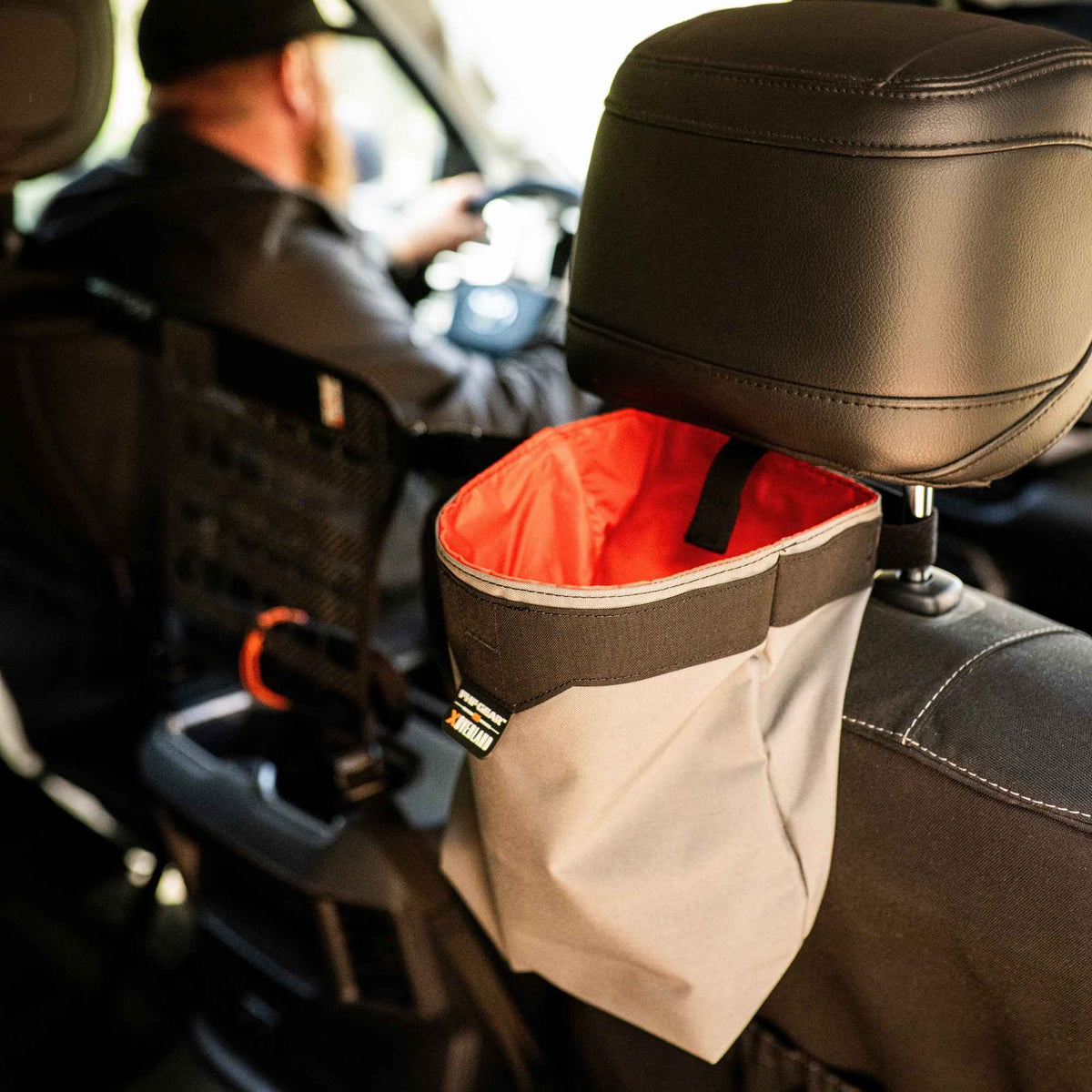 Grey storage bag with orange inside and FHF XOVERLAND branding on the center, it is mounted at the back of a headrest.