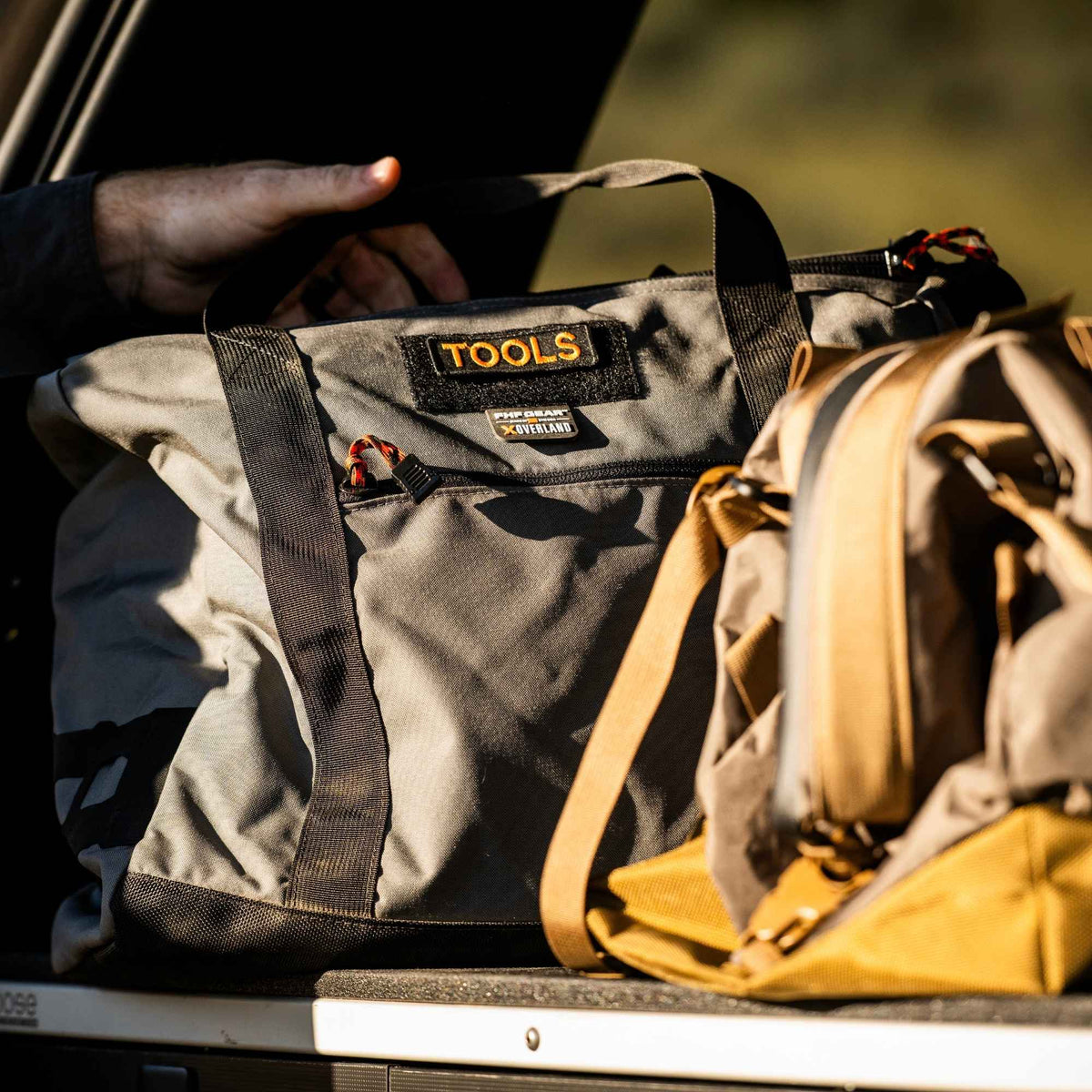 FHF The Stage Tote in grey in the back of a van and the hand of a man reaching out to it.