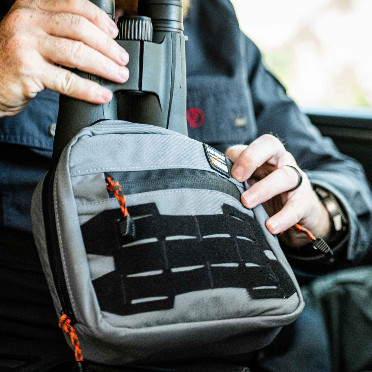 Man putting binoculars inside a grey Waypoint GP Pouch.