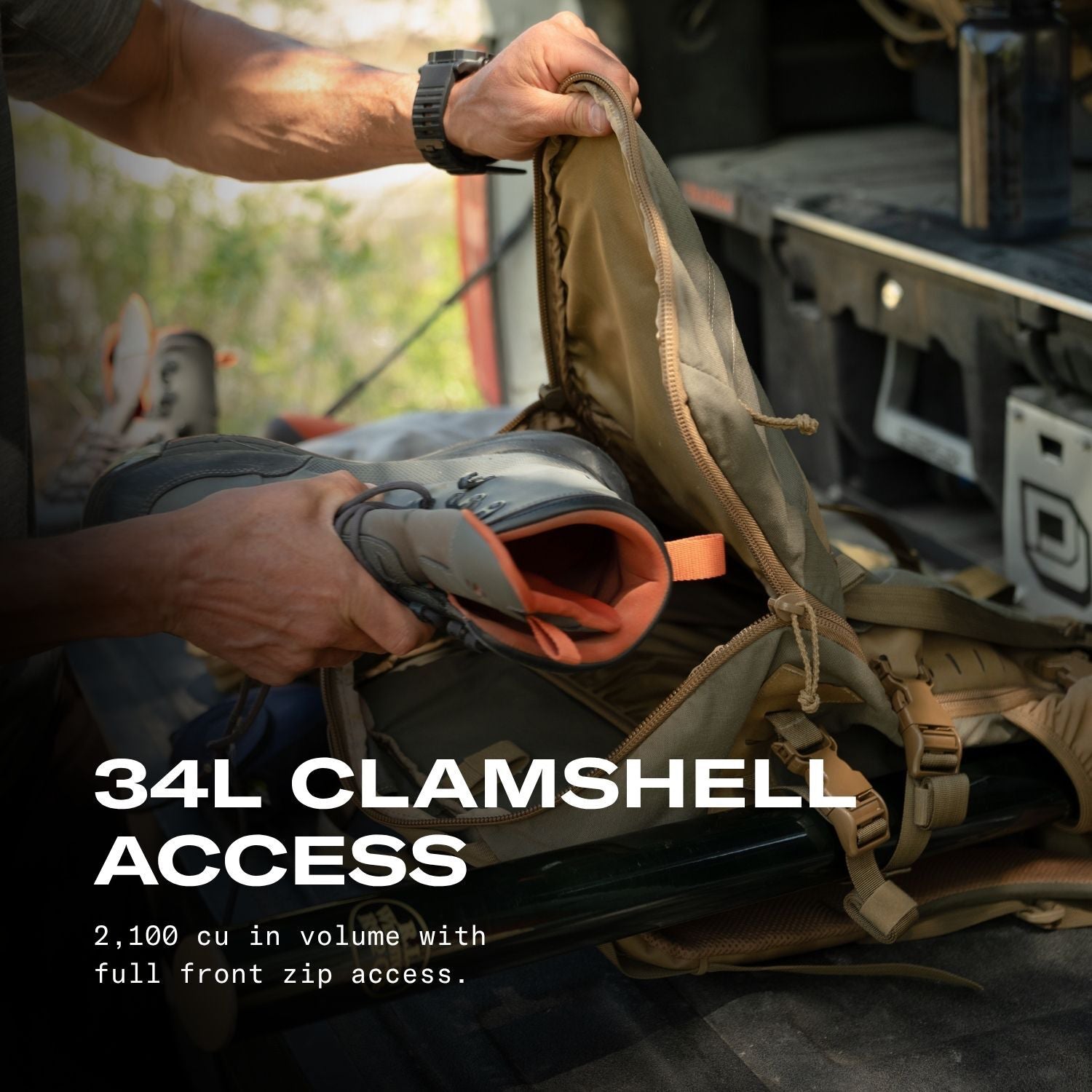 A close-up action shot of a person's hands opening a large tan backpack or gear bag with a zipper, while a hiking boot is being inserted. Large white text reads '34L CLAMSHELL ACCESS' with smaller descriptive text below, set against a dark outdoor vehicle or storage area background.