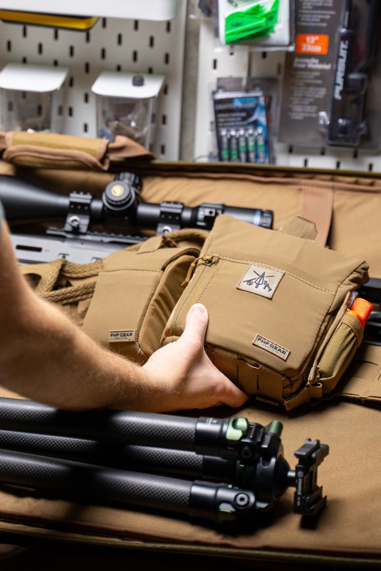 Person holding a tactical pouch with equipment on a pegboard background
