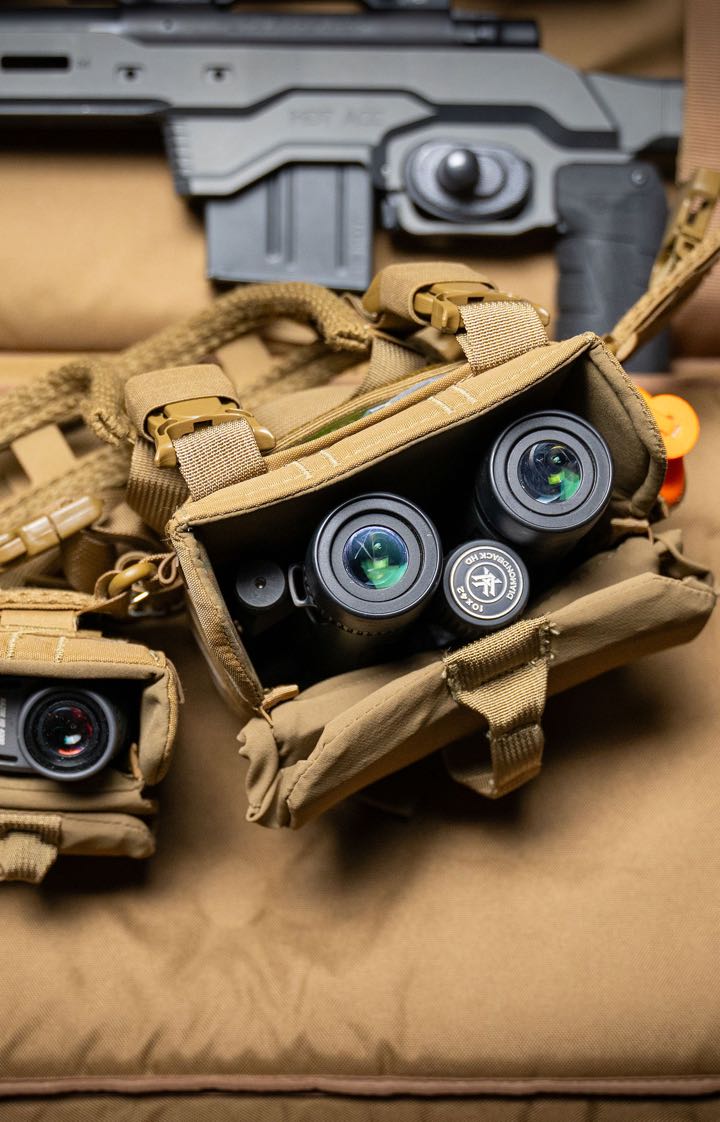 Coyote brown chest rig holding Diamondback HD 10x42 binoculars with green lenses.
