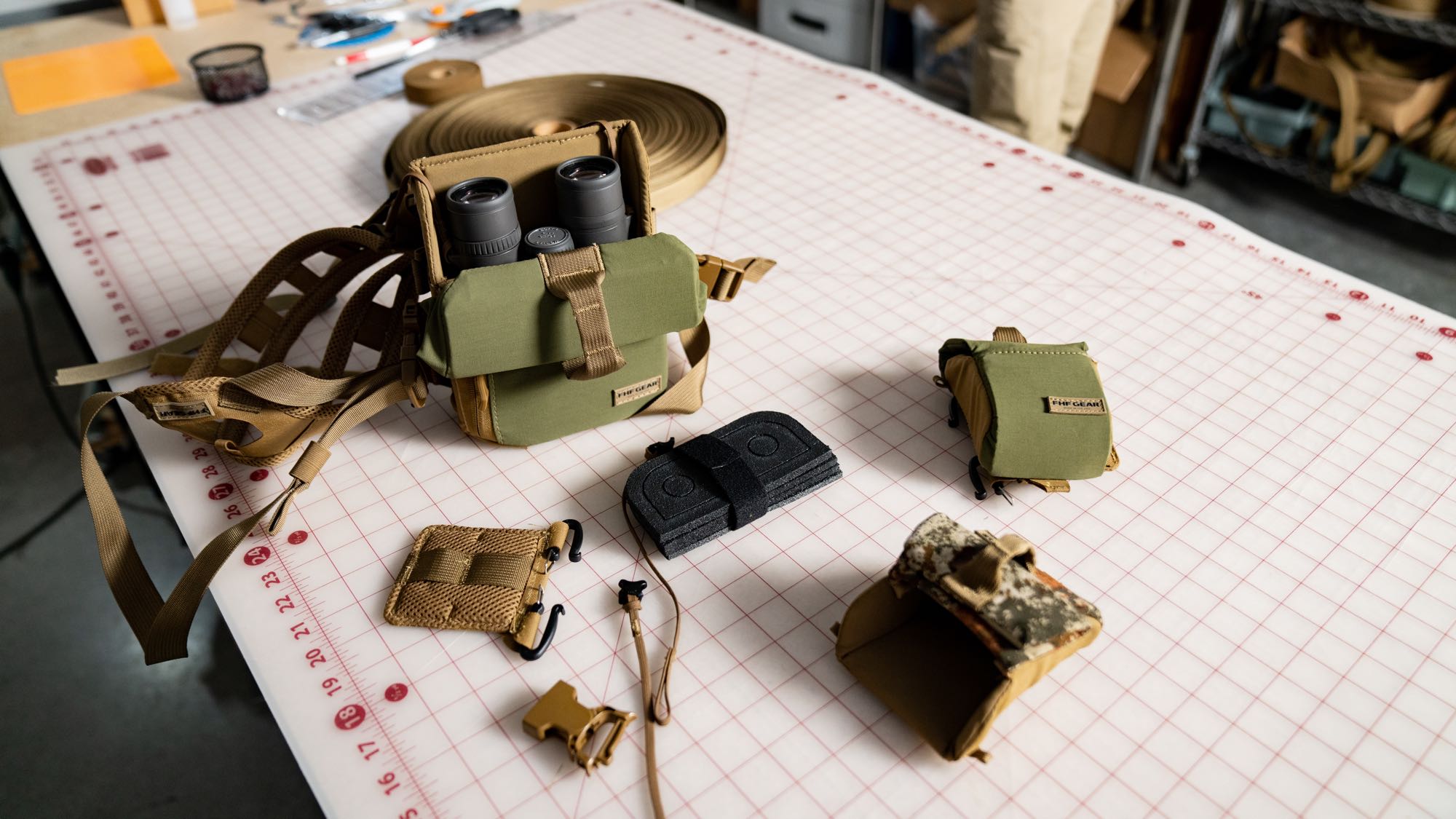 Olive green binocular chest harness with binoculars, chest straps, and accessory pouches.
